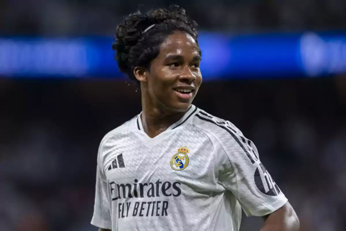 Jugador de fútbol con camiseta blanca del Real Madrid en el campo sonriendo.