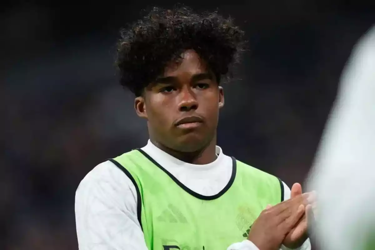 A young player in a green vest applauding in a stadium.