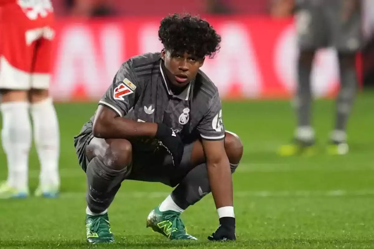 Un jugador de fútbol con uniforme gris se agacha en el campo durante un partido. Un jugador de fútbol con uniforme gris se agacha en el campo durante un partido.