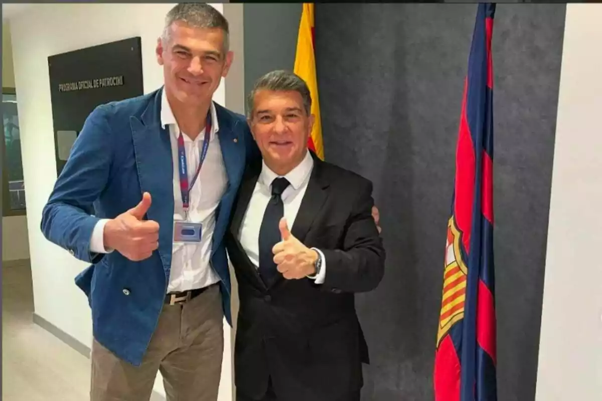 Two smiling men pose together with thumbs up in front of a flag and a sign in an office. Two smiling men pose together with thumbs up in front of a flag and a sign in an office.
