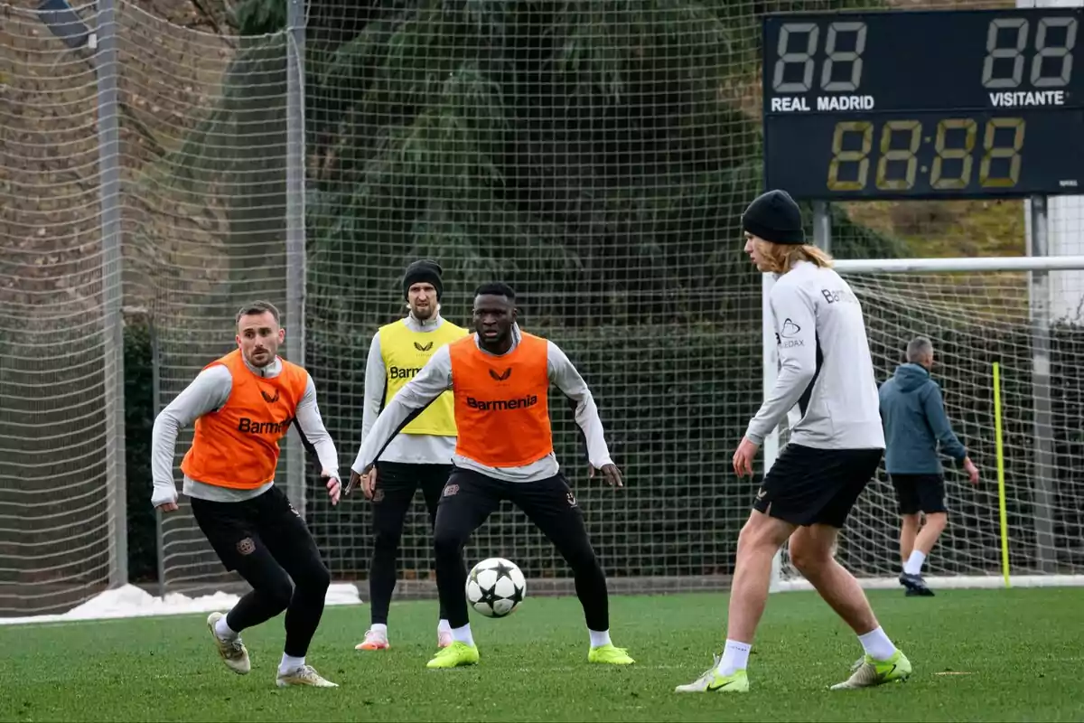 Joueurs de football s'entraînant sur un terrain avec des dossards orange et jaune et un tableau de bord en arrière-plan.