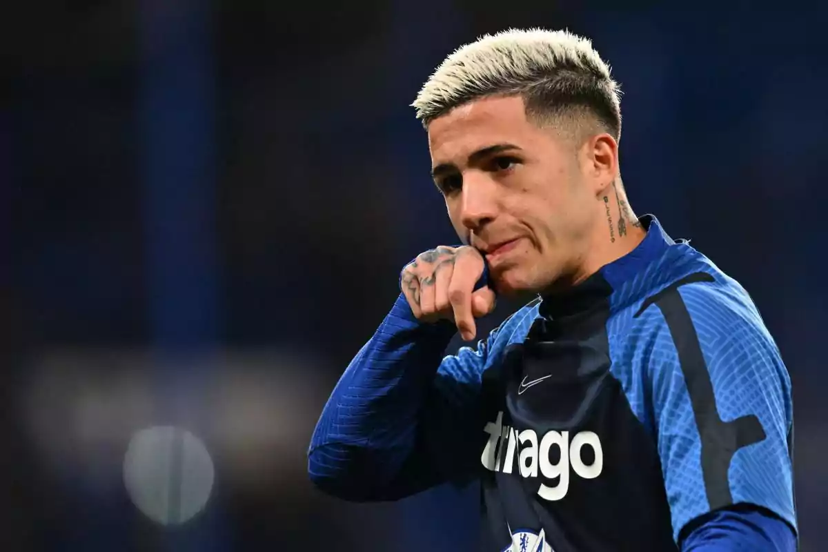 A player with blonde hair and tattoos on his hand, wearing a dark blue uniform, points forward on a playing field. A player with blonde hair and tattoos on his hand, wearing a dark blue uniform, points forward on a playing field.