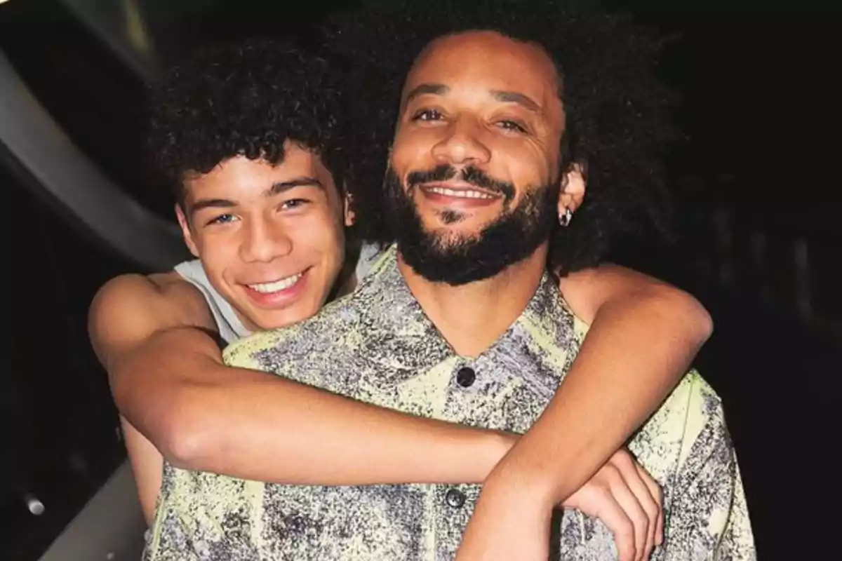 Two people smile as one hugs the other from behind in a dark setting. Two people smile as one hugs the other from behind in a dark setting.