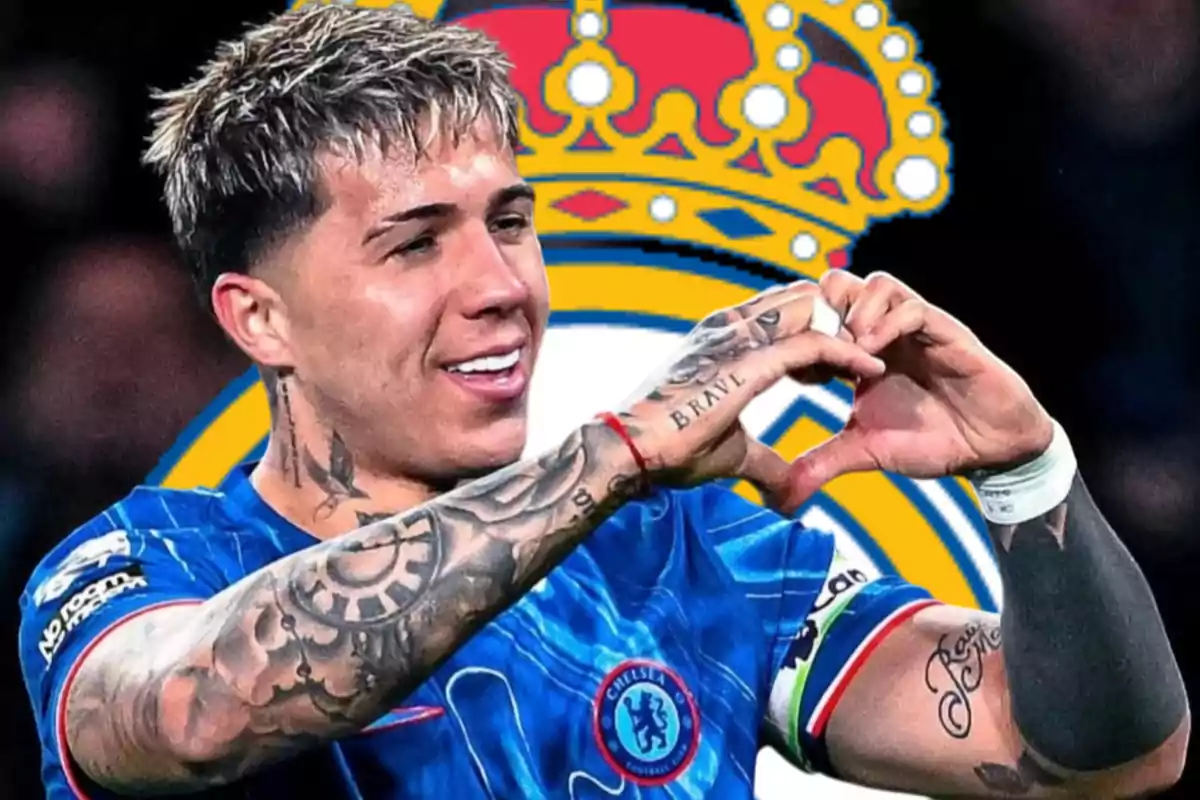 Un jugador de fútbol con tatuajes en los brazos hace un gesto de corazón con las manos, vistiendo una camiseta azul con un escudo de equipo, frente a un fondo con una corona.