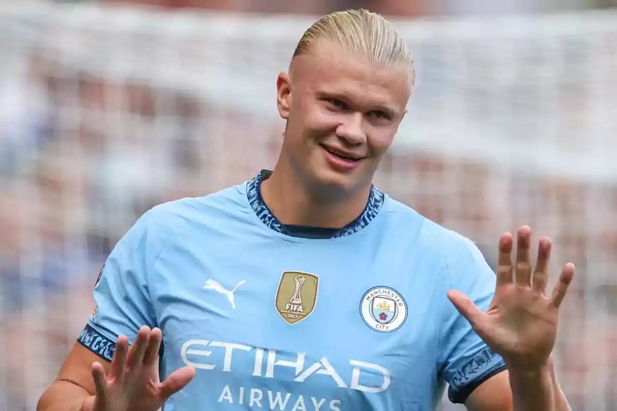 A soccer player in a light blue uniform smiles and raises his hands on a playing field. A soccer player in a light blue uniform smiles and raises his hands on a playing field.