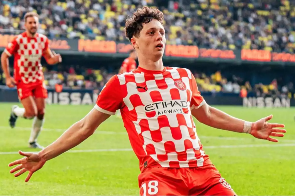 Soccer player celebrating a goal on the field in a red and white checkered uniform.