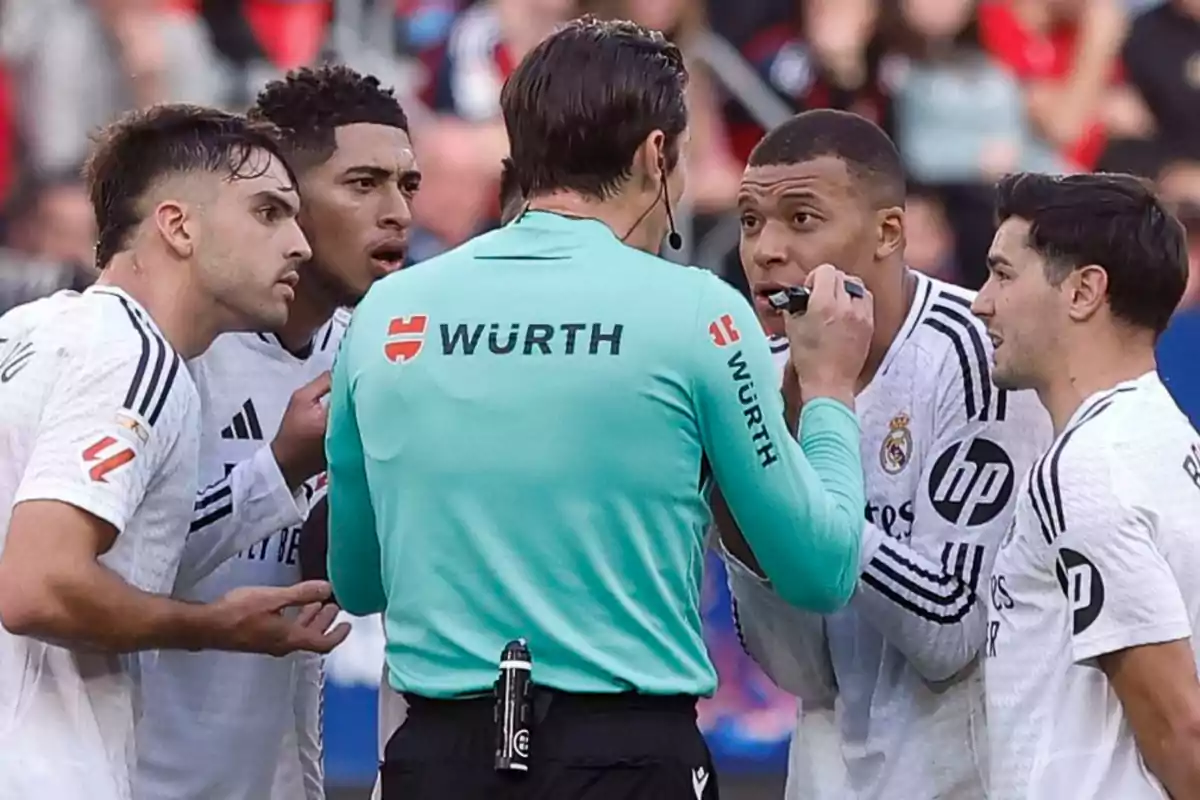 A soccer referee talks with several players dressed in white uniforms on the field.