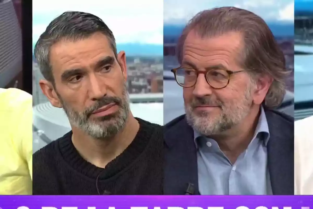 Two men with beards and gray hair are on a television show, one is wearing a black sweater and the other a blue jersey with a jacket, both seem to be in a serious conversation.