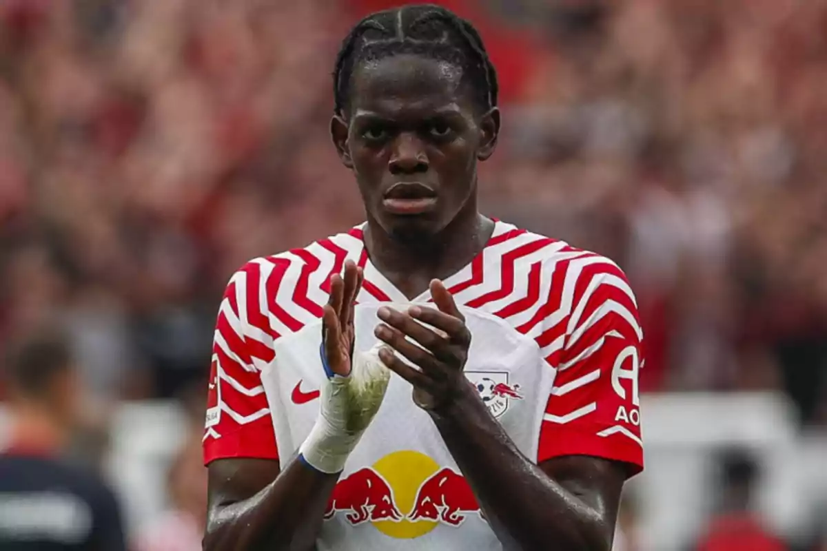 Jugador de fútbol aplaudiendo con uniforme blanco y rojo en un estadio.