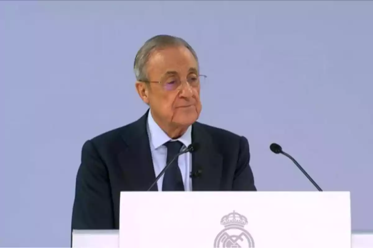 Hombre de traje hablando en un podio con el logo del Real Madrid.