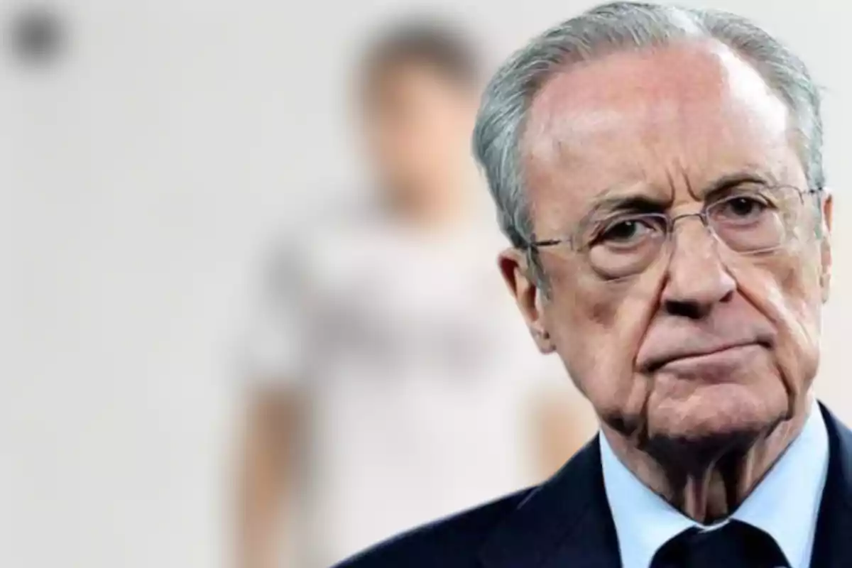 An elderly man with glasses and a serious expression in the foreground with a blurred figure in the background.