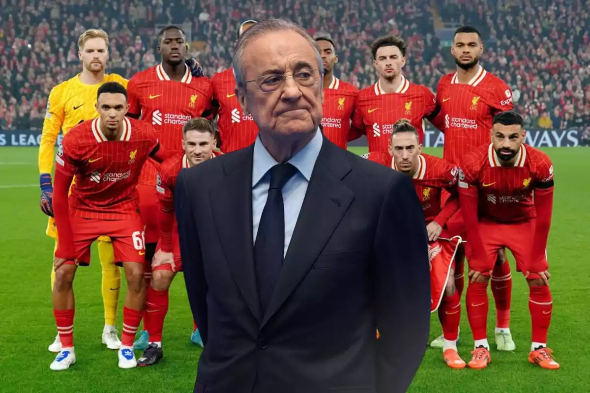 A man in a suit appears in the foreground in front of a soccer team in red uniforms posing on the field before a match.