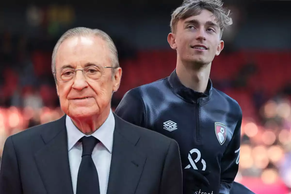 Two people posing in a soccer stadium, one of them wearing a formal suit and the other dressed in a sports uniform.