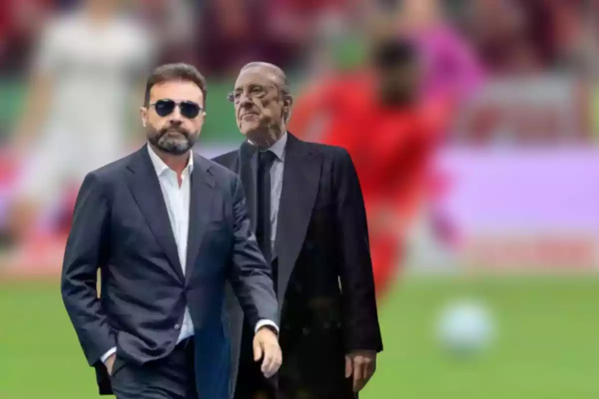 Two men dressed in suits on a soccer field, one wearing sunglasses and the other having grey hair.