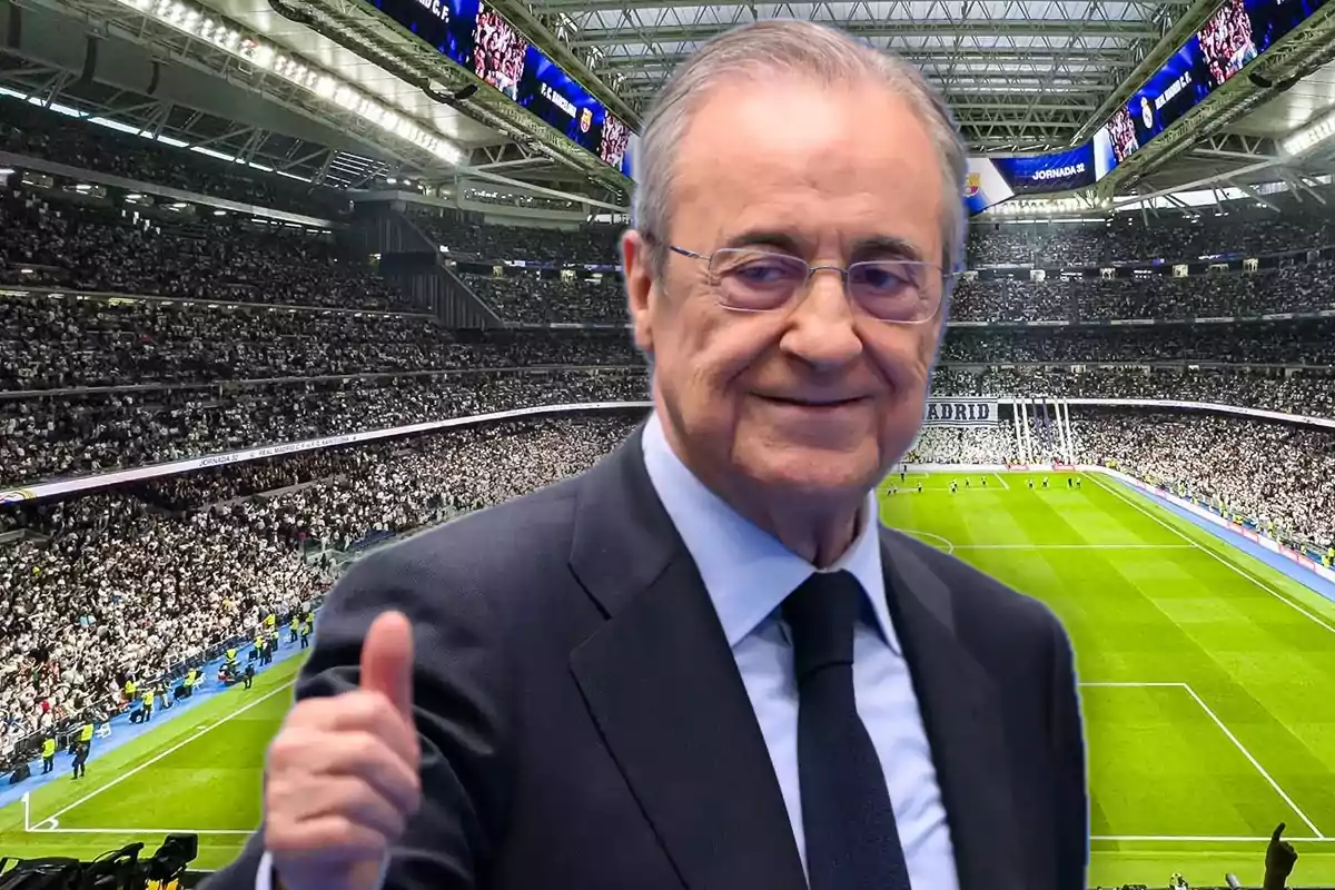 Hombre de traje sonriente levantando el pulgar en un estadio de fútbol lleno de aficionados