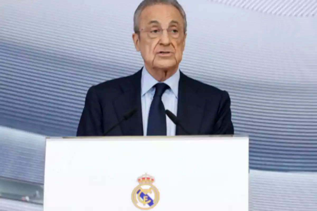 A man in a suit speaking at a podium with the Real Madrid crest. A man in a suit speaking at a podium with the Real Madrid crest.