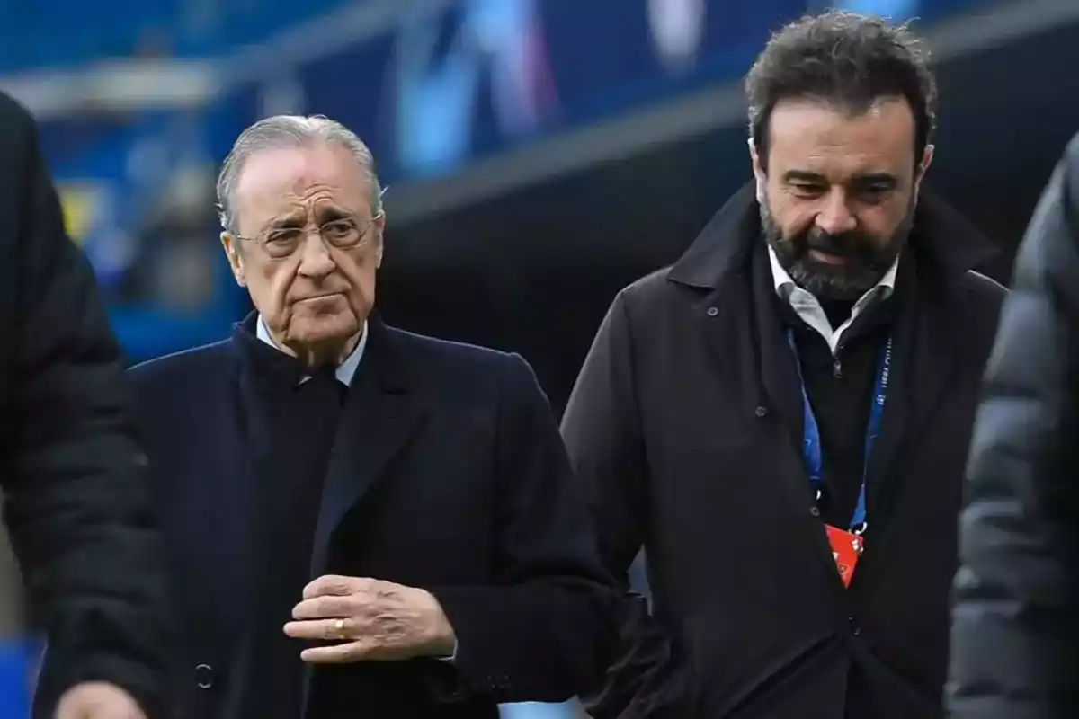 Dos hombres caminando juntos en un estadio con expresión seria.