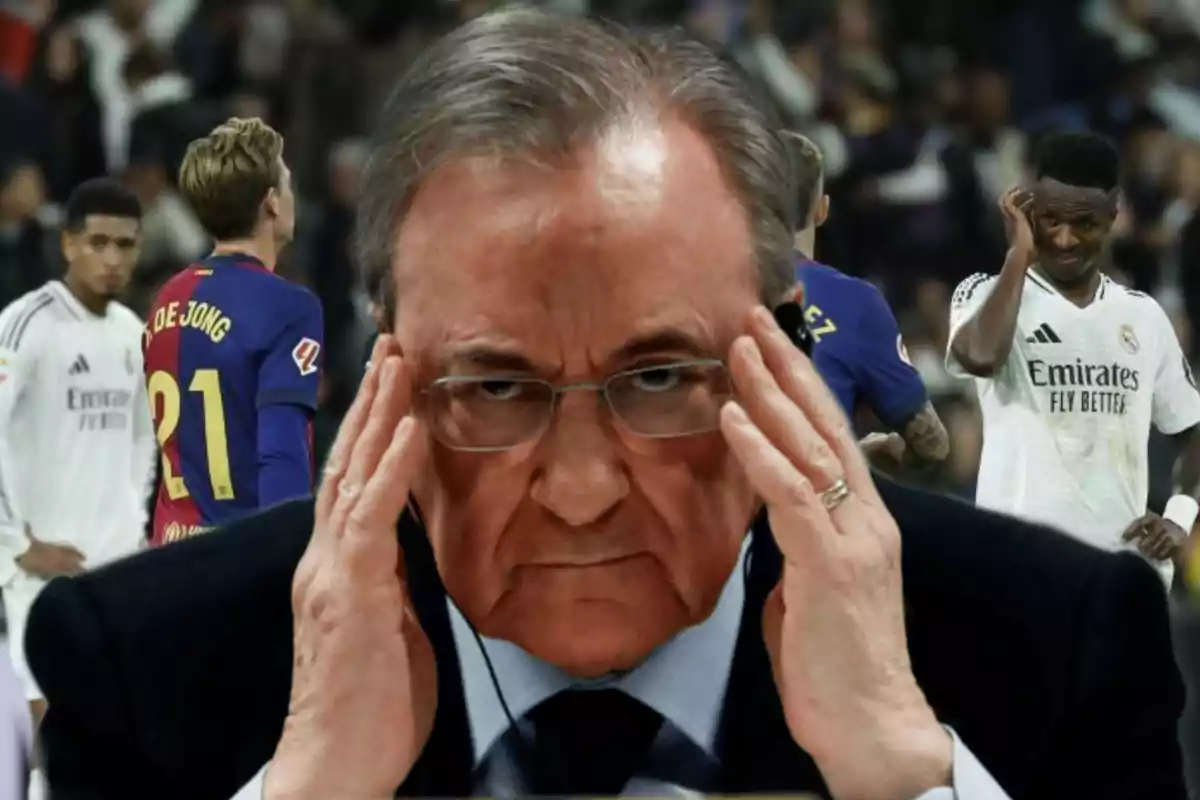 A man with glasses and a serious expression touches his head, while in the background soccer players can be seen on a field.