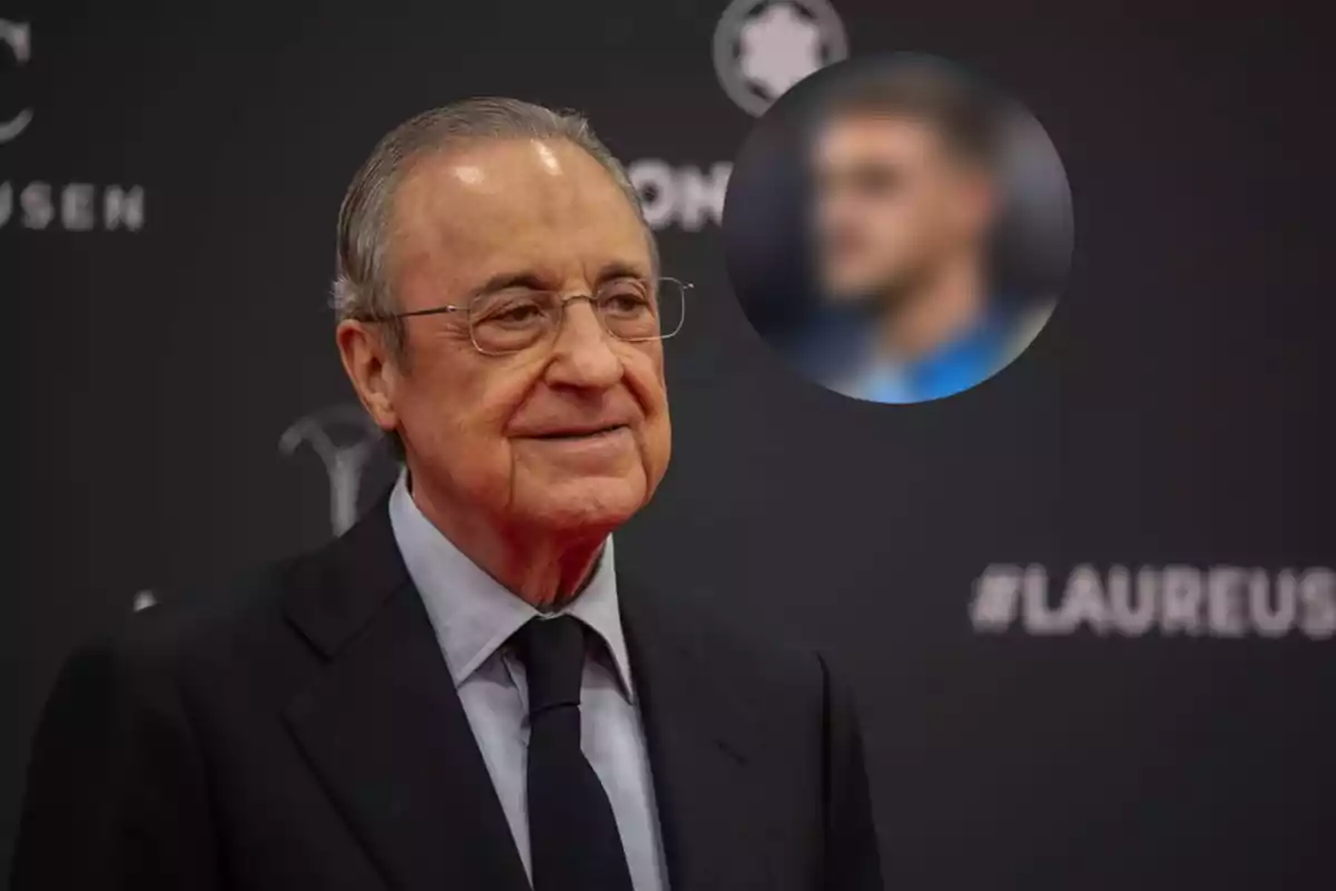 An older man with glasses and a dark suit smiles at an event with a black background and logos.