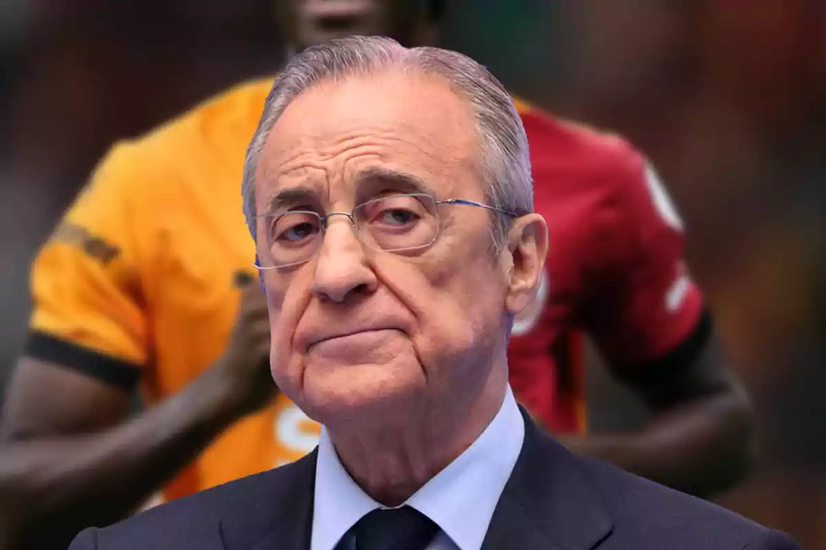 Older man with glasses and a serious expression in front of a blurred background with people wearing yellow and red sports jerseys
