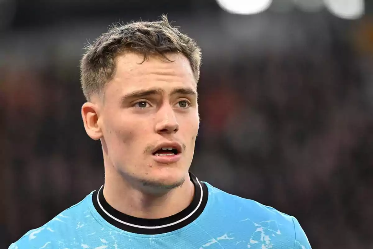 A young man with a serious expression wears a light blue t-jersey with black and white details, with an out-of-focus background. A young man with a serious expression wears a light blue t-jersey with black and white details, with an out-of-focus background.