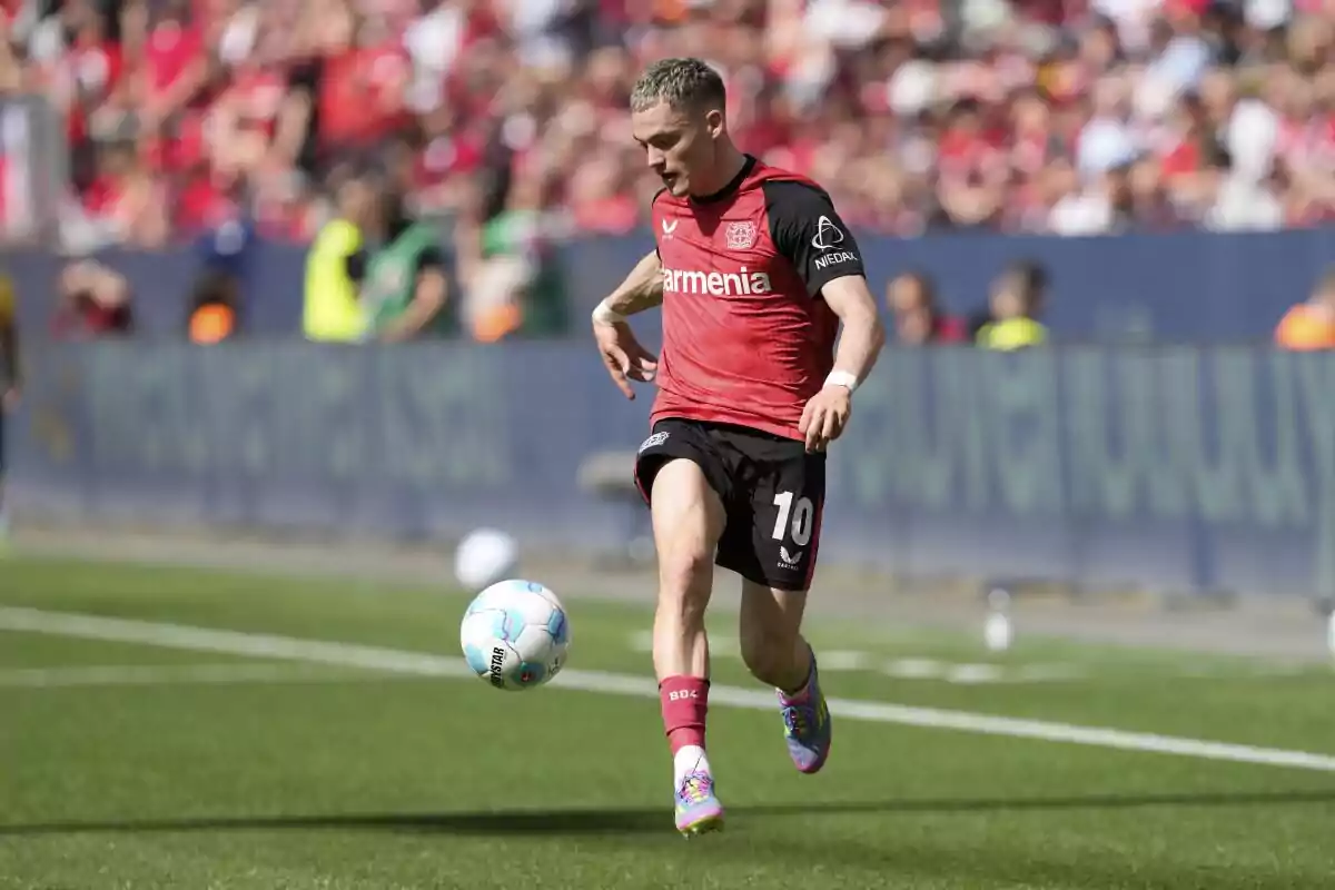 Soccer player in a red and black uniform controlling the ball during a match in front of a crowd in the stands Soccer player in a red and black uniform controlling the ball during a match in front of a crowd in the stands