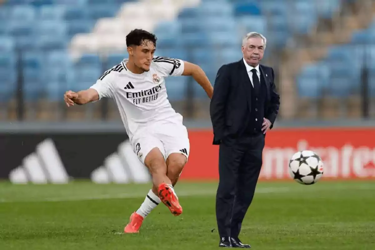 Un jugador de fútbol en acción junto a un hombre de traje en el campo de juego.