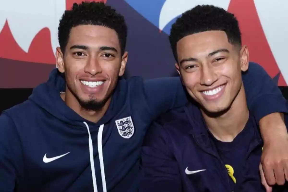 Dos personas sonriendo y abrazándose, ambas llevan sudaderas deportivas con logotipos. Dos personas sonriendo y abrazándose, ambas llevan sudaderas deportivas con logotipos.