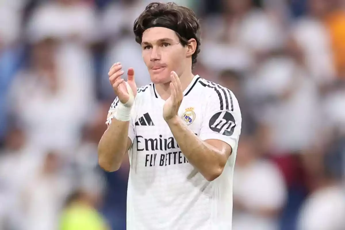 Football player applauding on the field in white Real Madrid uniform.