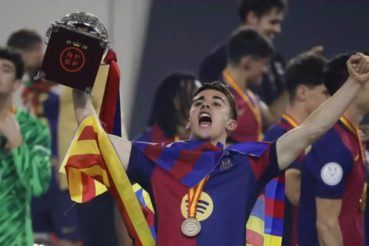 Player celebrating with a medal and a trophy while carrying a flag on his shoulders at a sporting event.