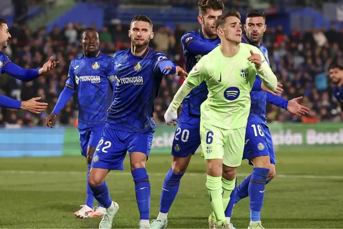 Jugadores de fútbol en acción durante un partido, con un equipo vistiendo uniforme azul y el otro uniforme verde claro.