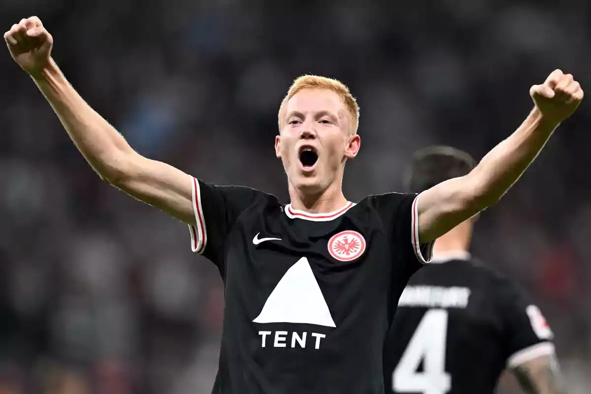 A player in a black uniform celebrates with arms raised in a stadium. A player in a black uniform celebrates with arms raised in a stadium.