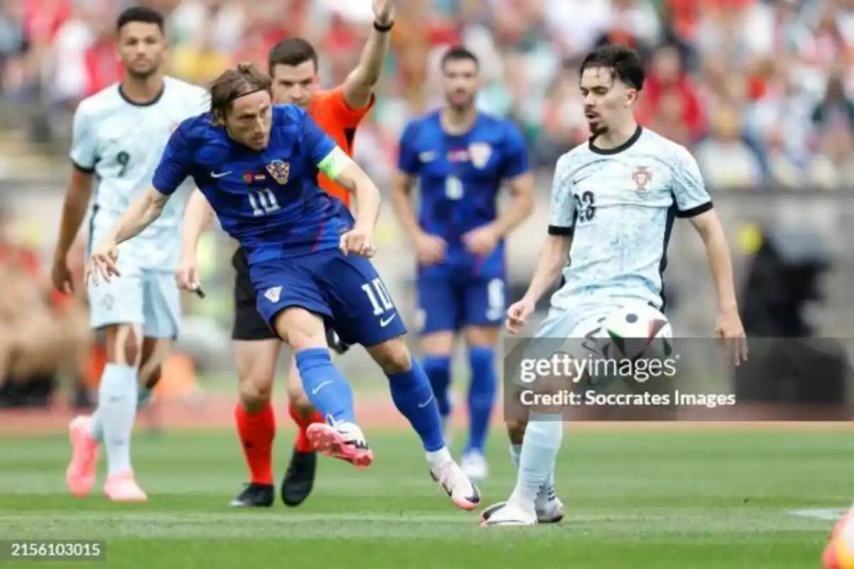 Futbolistas de Croacia y Portugal disputan el balón durante un partido mientras el árbitro observa la jugada en el campo Futbolistas de Croacia y Portugal disputan el balón durante un partido mientras el árbitro observa la jugada en el campo