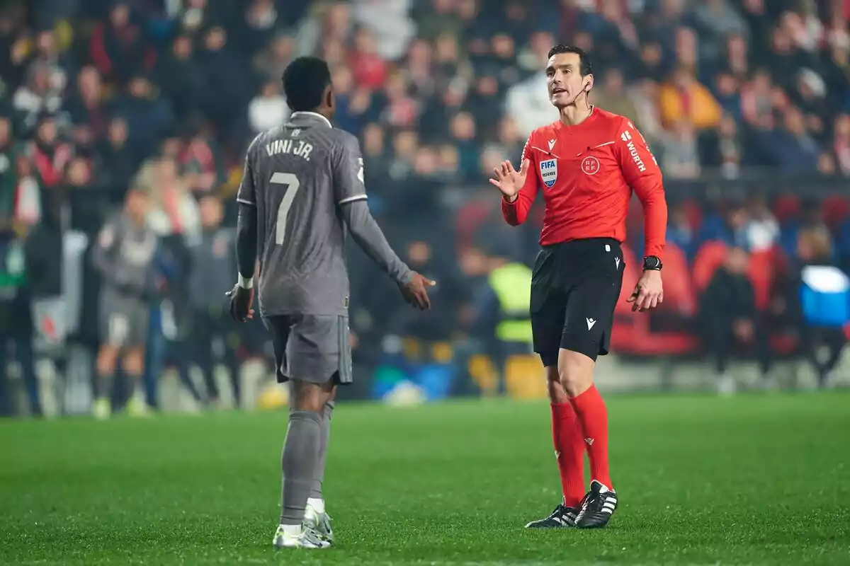 Un árbitro de fútbol dialoga con un jugador en el campo durante un partido.