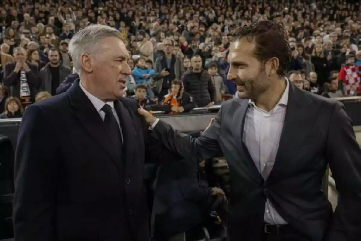 Dos hombres de traje se saludan amistosamente en un estadio lleno de espectadores.