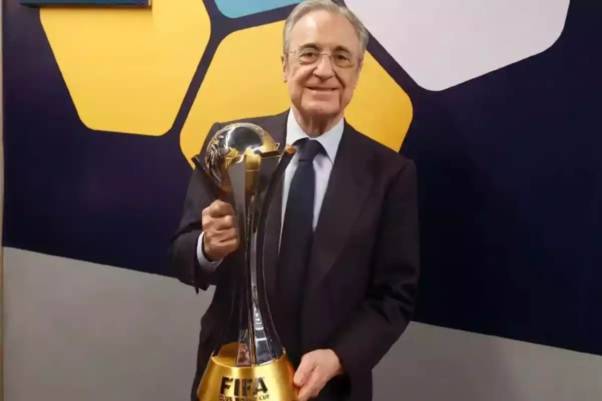 Un hombre con traje sosteniendo un trofeo de la FIFA frente a un fondo colorido.