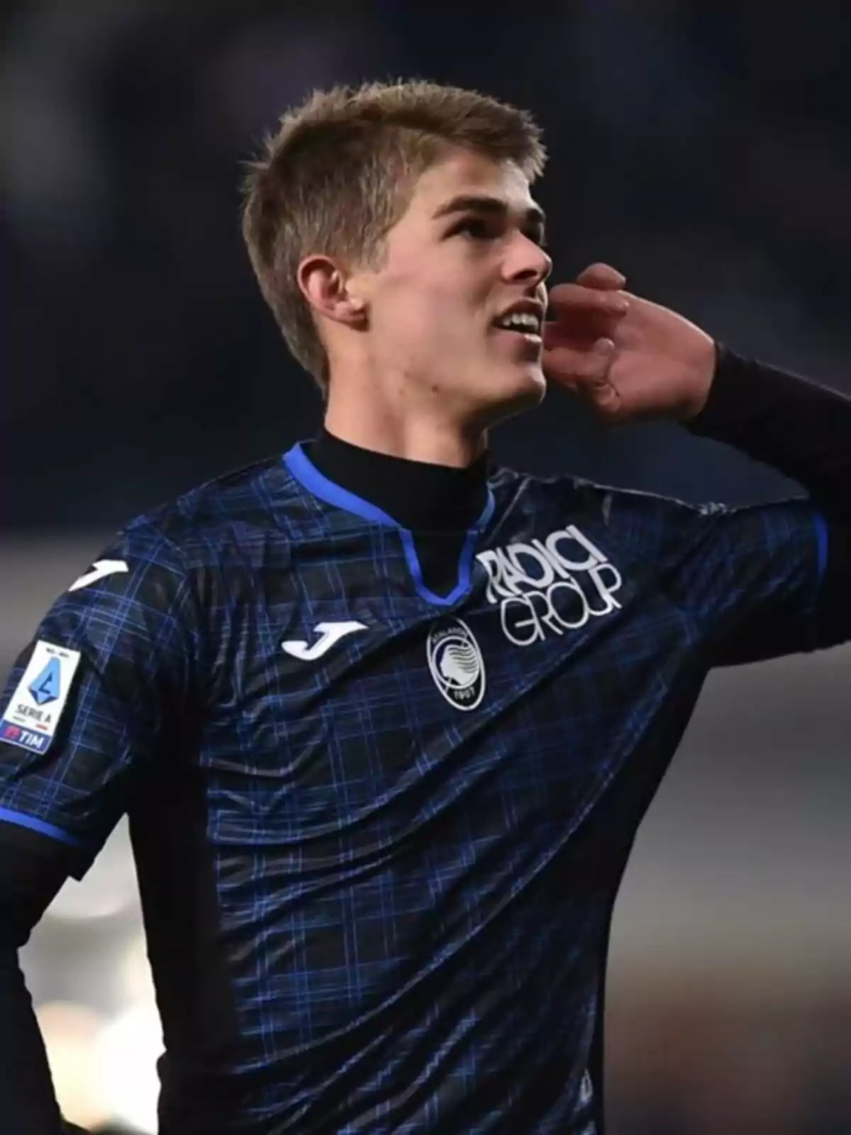 Jugador de fútbol con uniforme azul y negro celebrando en el campo.