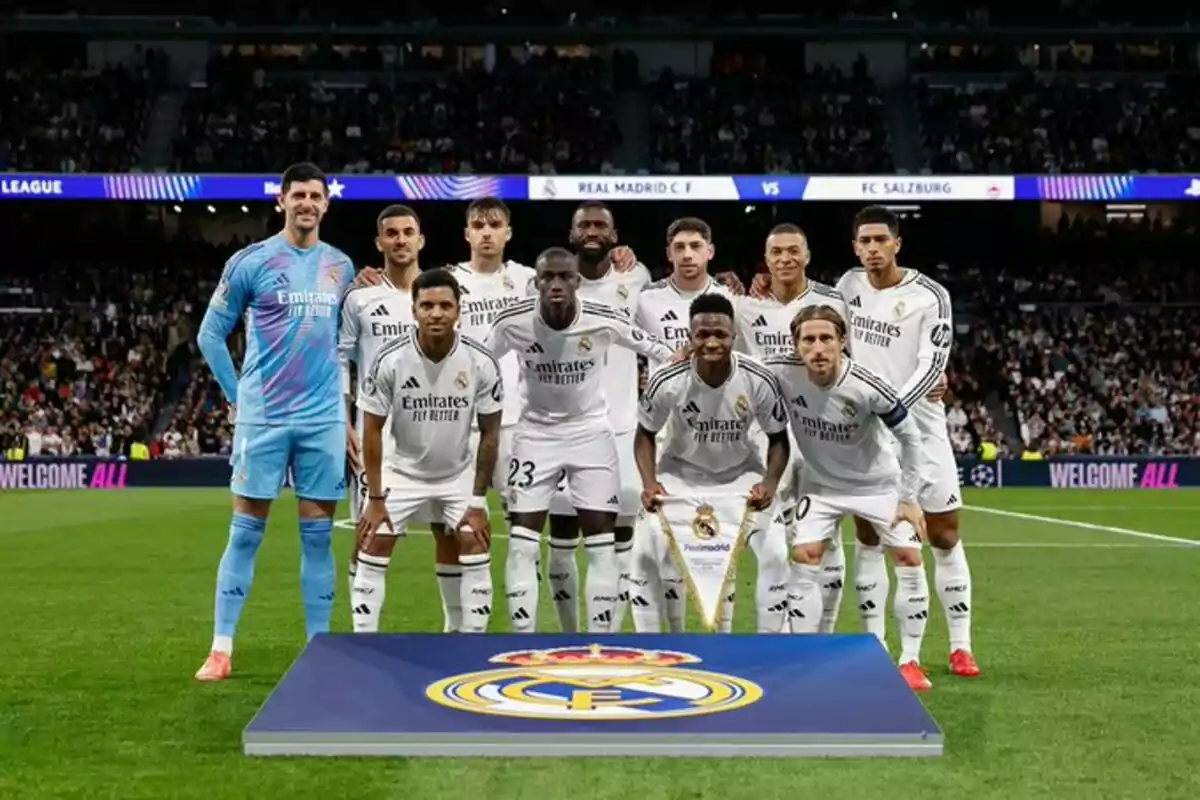 Un equipo de fútbol posando en el campo antes de un partido con el escudo del club en primer plano.