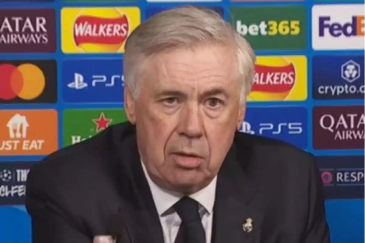 A man at a press conference with a background of sports sponsor logos.