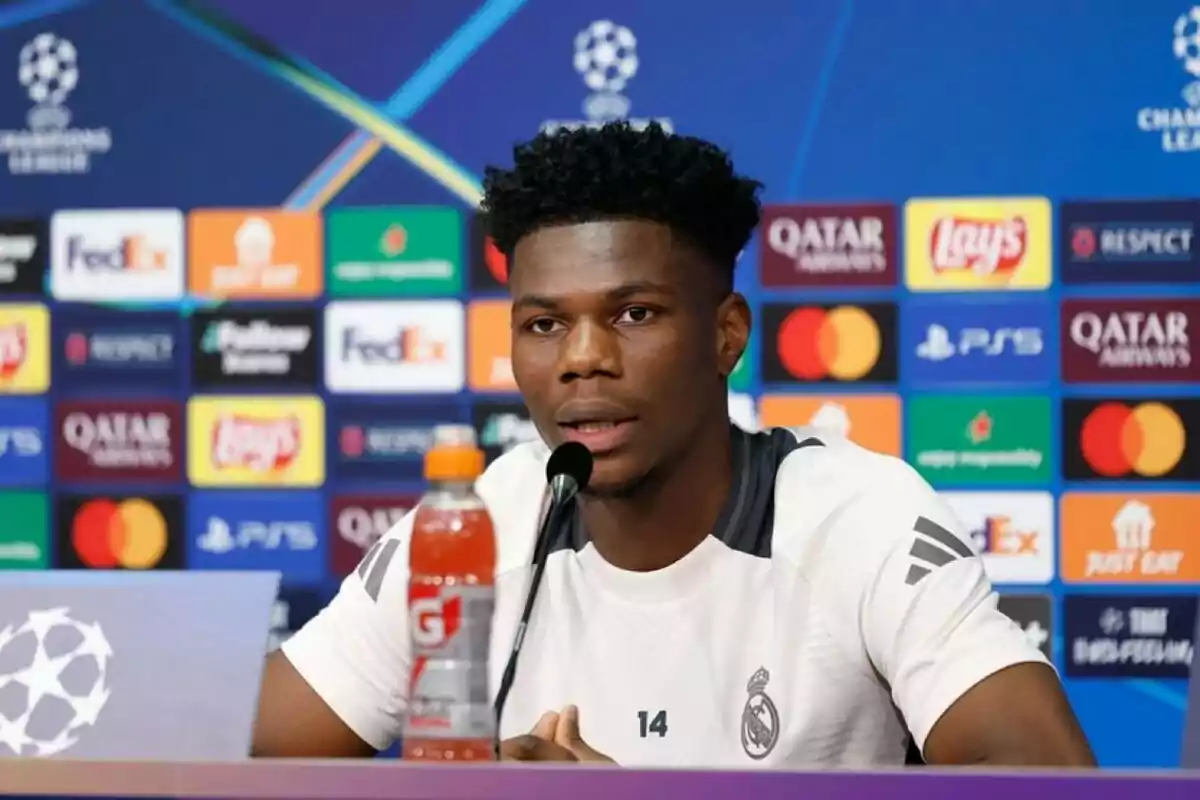 A player at a press conference with a background of Champions League logos.