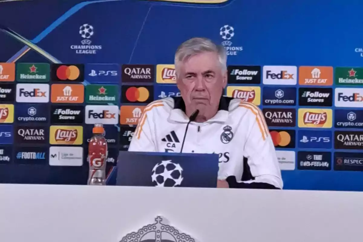 A man at a UEFA Champions League press conference with a sponsors' backdrop.