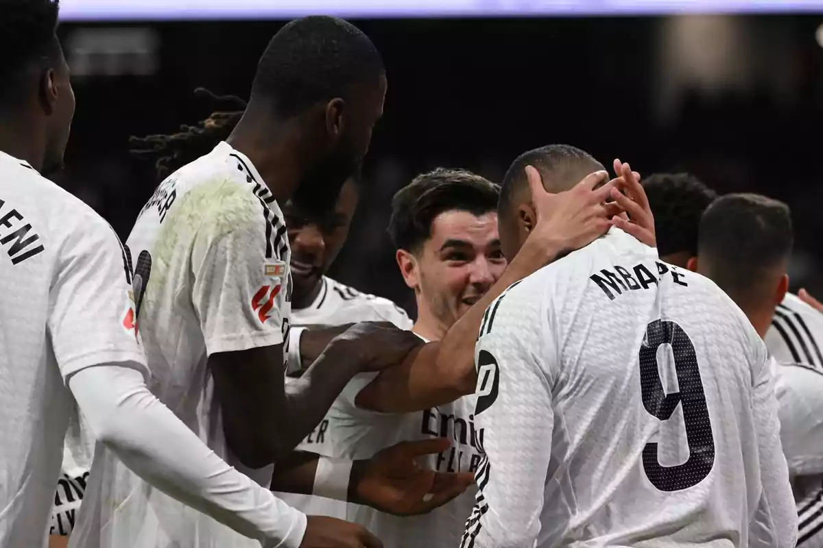 Soccer players celebrate a goal by hugging on the field while wearing white uniforms. Soccer players celebrate a goal by hugging on the field while wearing white uniforms.