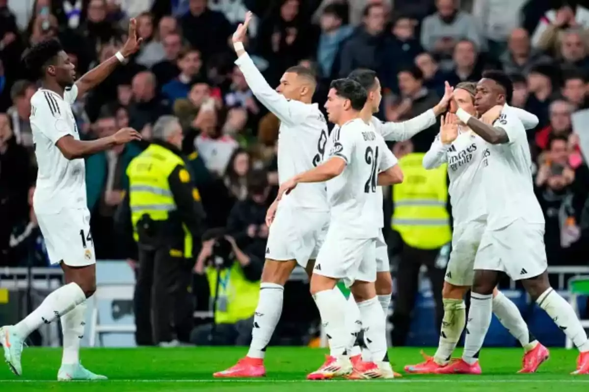 Soccer players in white uniforms celebrate on the field during a match, surrounded by spectators and security personnel. Soccer players in white uniforms celebrate on the field during a match, surrounded by spectators and security personnel.