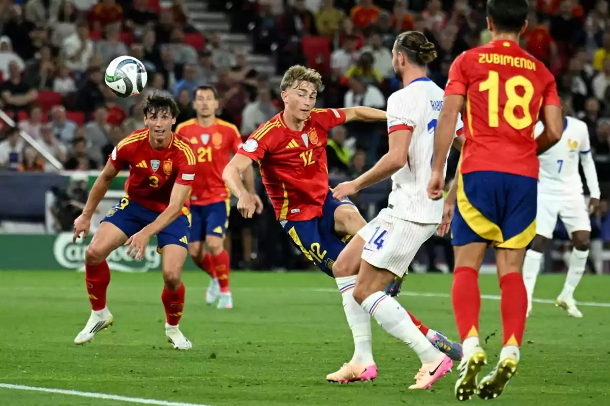 Players from the Spain and France national teams compete for the ball during a soccer match in a stadium full of spectators. Players from the Spain and France national teams compete for the ball during a soccer match in a stadium full of spectators.