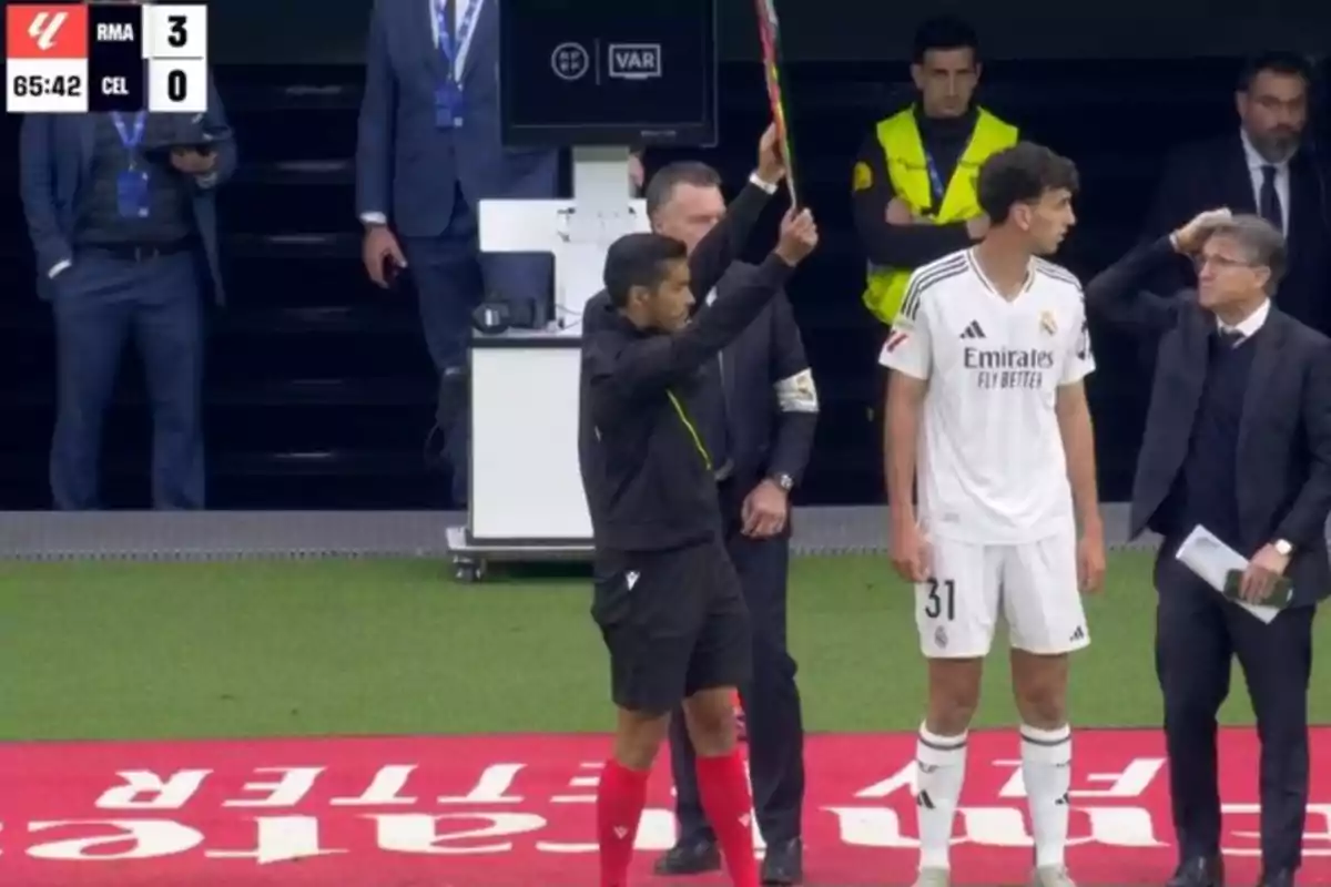 An assistant referee holds a substitution board while a Real Madrid player waits to enter the field during a soccer match, with the scoreboard showing 3-0 in favor of Real Madrid. An assistant referee holds a substitution board while a Real Madrid player waits to enter the field during a soccer match, with the scoreboard showing 3-0 in favor of Real Madrid.