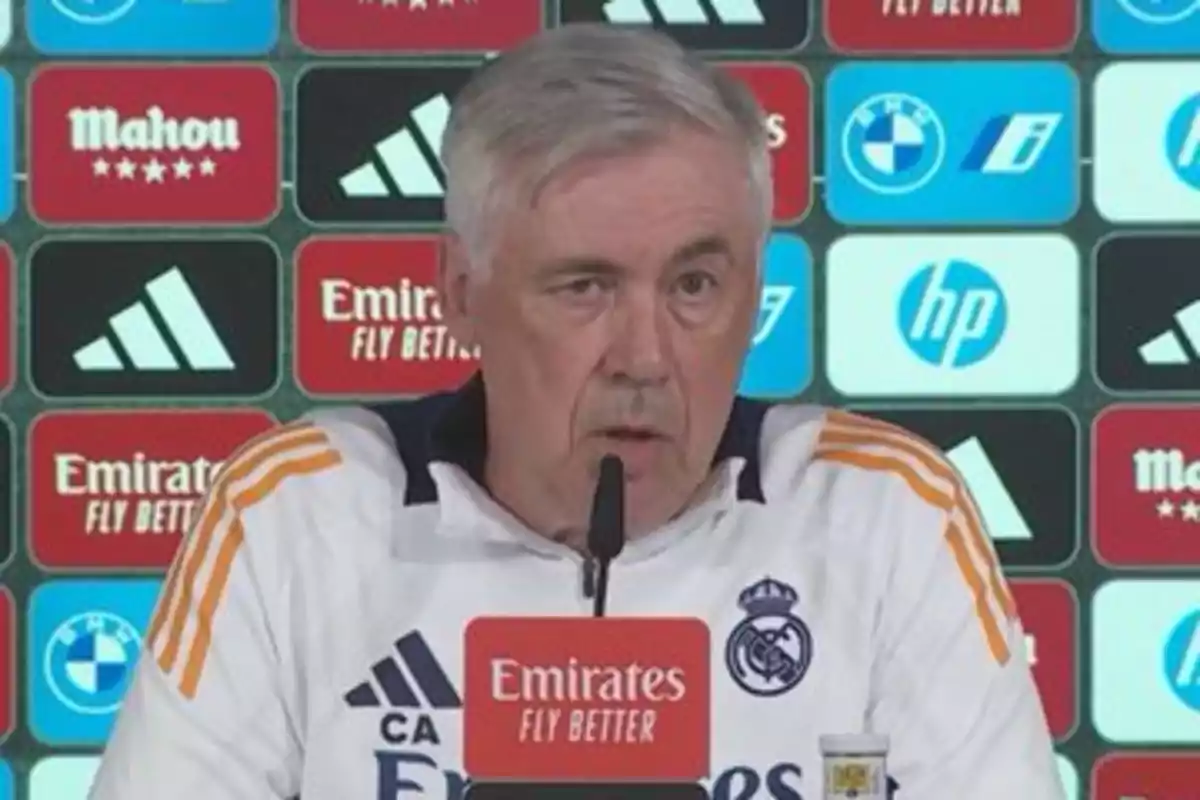 A man at a press conference with a background of sponsor logos.