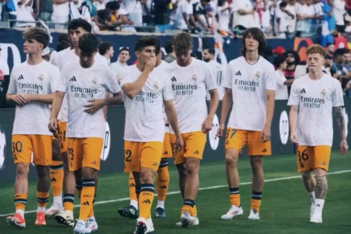 A group of players in white and orange uniforms walks across the field while the crowd watches from the stands. A group of players in white and orange uniforms walks across the field while the crowd watches from the stands.