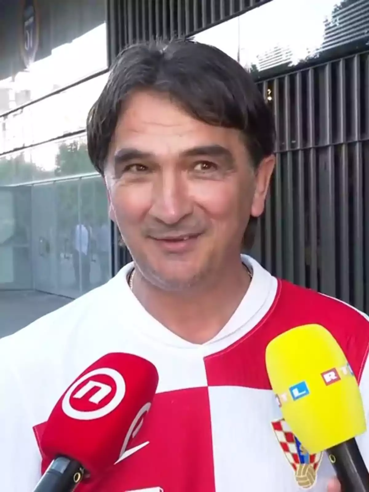 Un hombre con una camiseta de cuadros rojos y blancos está siendo entrevistado por varios micrófonos de diferentes medios de comunicación. Un hombre con una camiseta de cuadros rojos y blancos está siendo entrevistado por varios micrófonos de diferentes medios de comunicación.