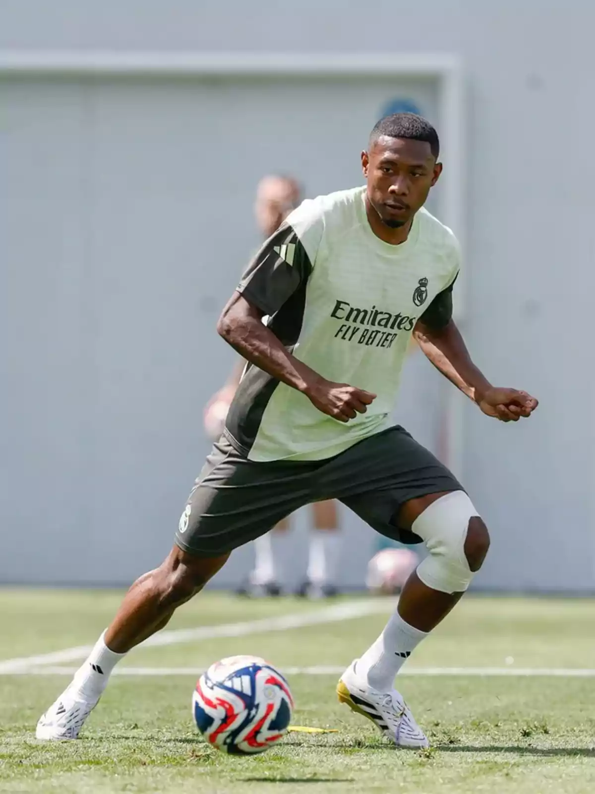 Futbolista entrenando en campo de césped con vendaje en la rodilla y balón cerca de sus pies Futbolista entrenando en campo de césped con vendaje en la rodilla y balón cerca de sus pies