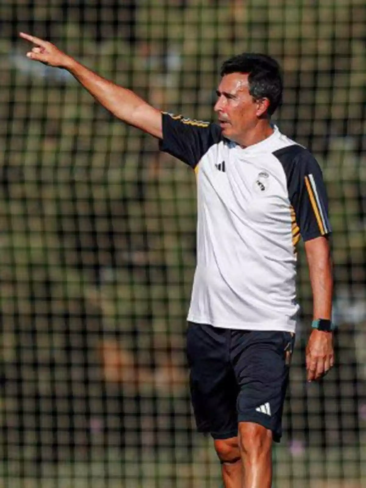 Entrenador de fútbol con uniforme blanco y negro señalando con el brazo extendido durante una práctica en campo